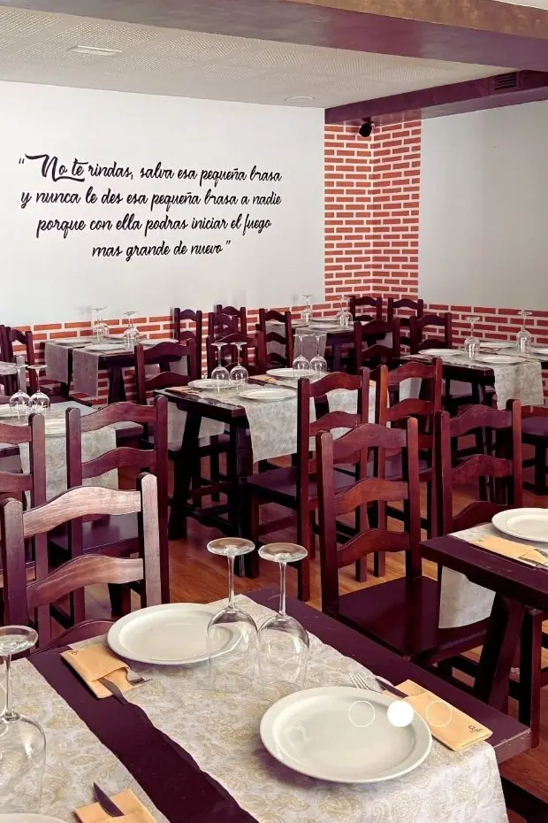 Comedor del restaurante con mesas de madera, manteles claros y zócalo de ladrillo